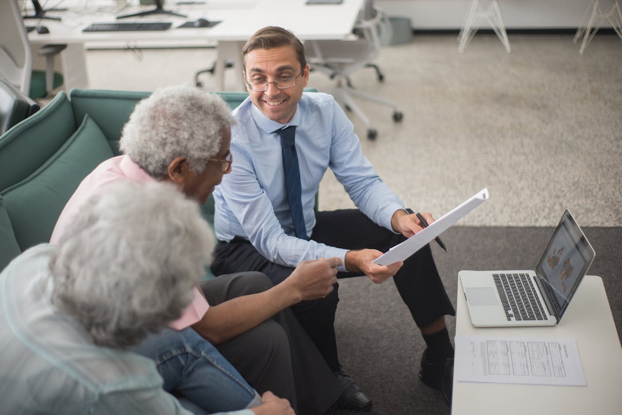 Services-01 Consultant discussing financial plans with senior clients in a modern office setting, using documents and a laptop.